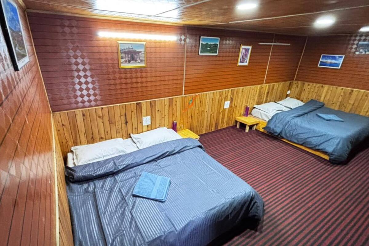A room with wooden walls, two beds, a small table, and a red carpet.