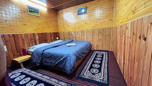 A wooden-paneled room with a bed, a small table, and a rug. - Zenden Stay And Cafe (Jibhi)