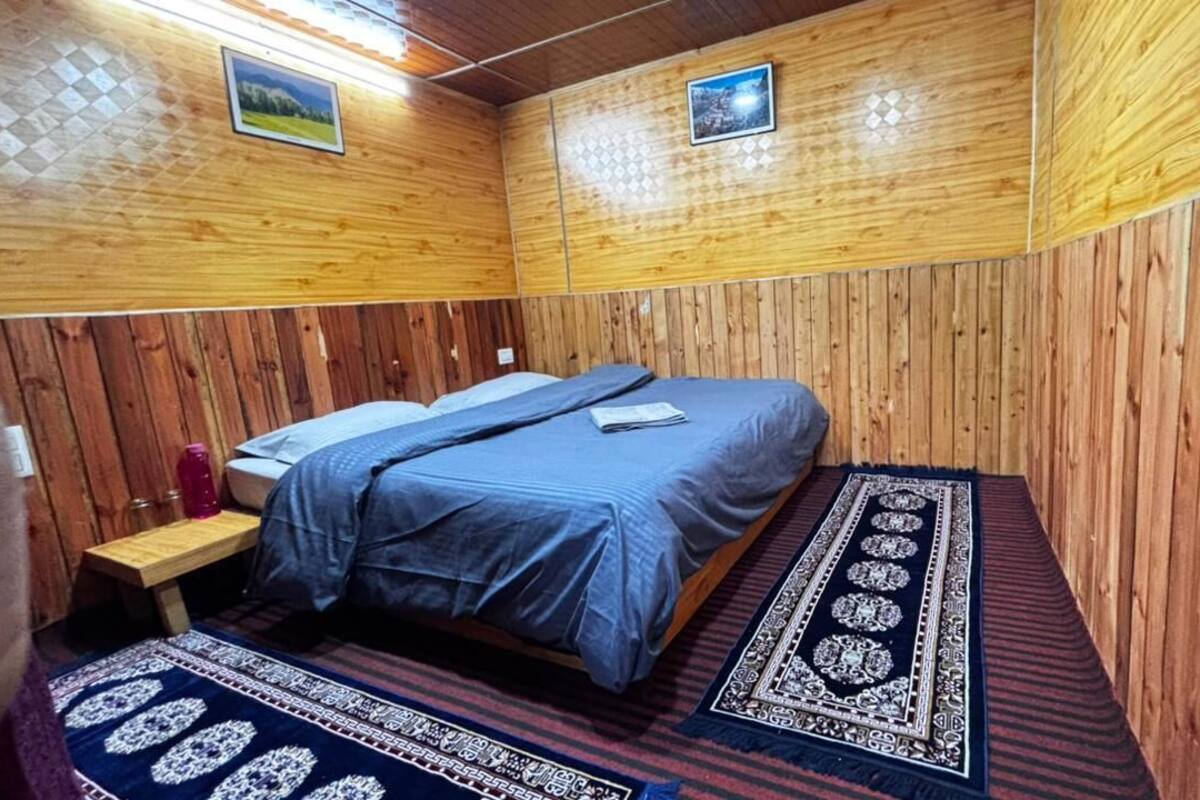 A wooden-paneled room with a bed, a small table, and a rug.