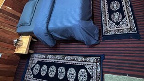 A compact room with a bed, a small table, a decorative rug, and a framed picture on the wall. - Zenden Stay And Cafe (Jibhi)