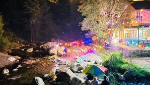 A riverside campsite with tents, a dining area, and a building with string lights. - Zenden Stay And Cafe (Jibhi)