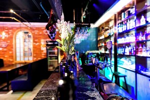 Un bar con una barra larga, un jarrón con flores y estantes con botellas.