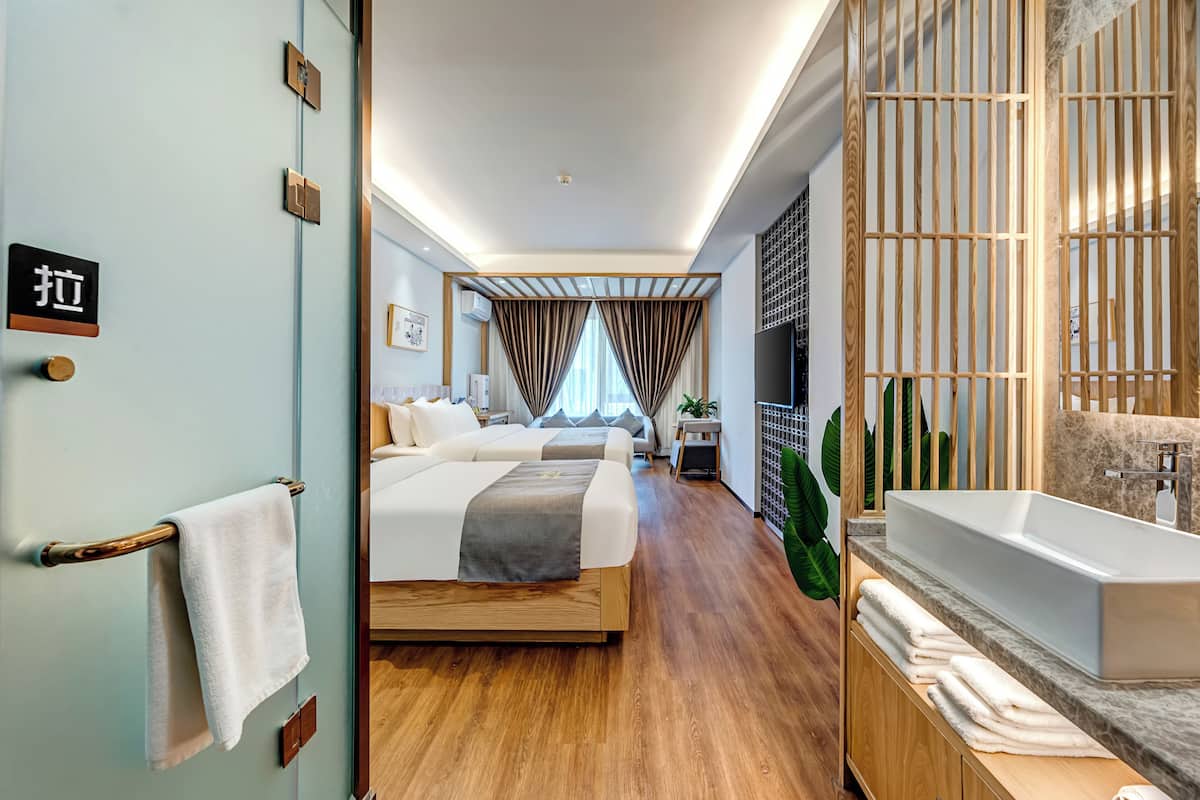 Una habitación de hotel moderna con una cama grande, un área de descanso separada, un baño con bañera y vistas a la ciudad.