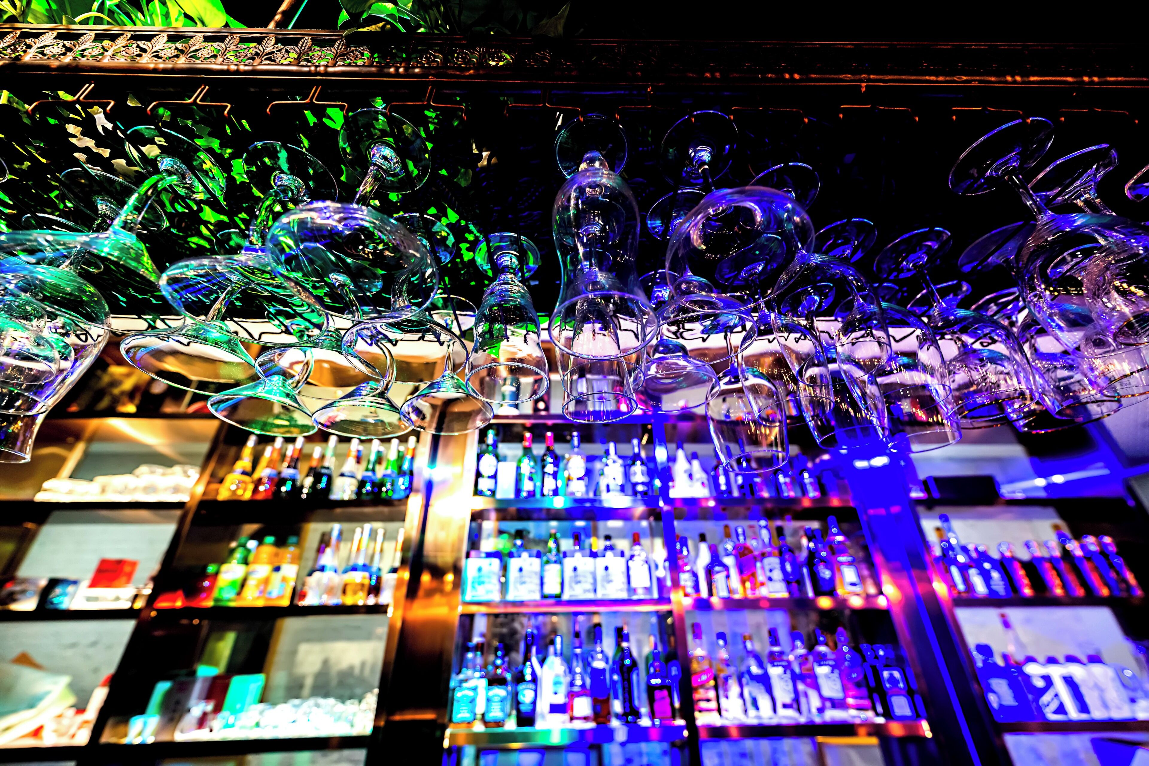 A bar area with shelves stocked with various bottles and a collection of wine glasses hanging above.