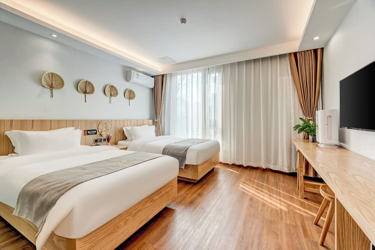 Habitación de hotel con dos camas, un escritorio, un televisor y un ventanal con cortinas.