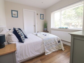 A bedroom with a bed, a bedside table, a window with blinds, and a door. - Cross Winds (Lancaster)