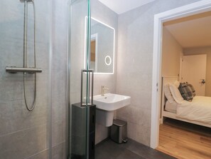 A modern bathroom with a glass-enclosed shower, a white sink, and a mirror with a light. - Cross Winds (Lancaster)