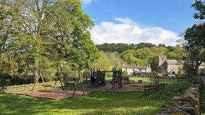 A park with playground equipment, a stone wall, and a building in the background. - Cross Winds (Lancaster)