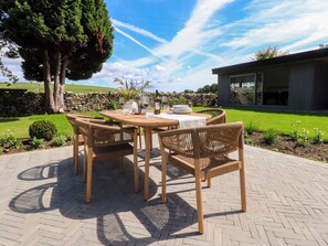 An outdoor dining area with a table and chairs, surrounded by a stone wall and greenery. - Cross Winds (Lancaster)