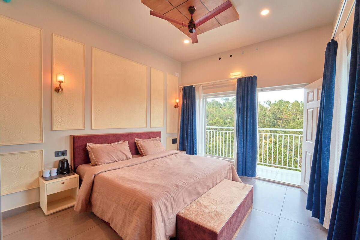 A bedroom with a large bed, bedside tables, a bench, a ceiling fan, and a balcony with curtains.