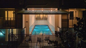 Una piscina con cerramiento de vidrio, rodeada por una valla metálica y una escalera que conduce a un nivel superior.