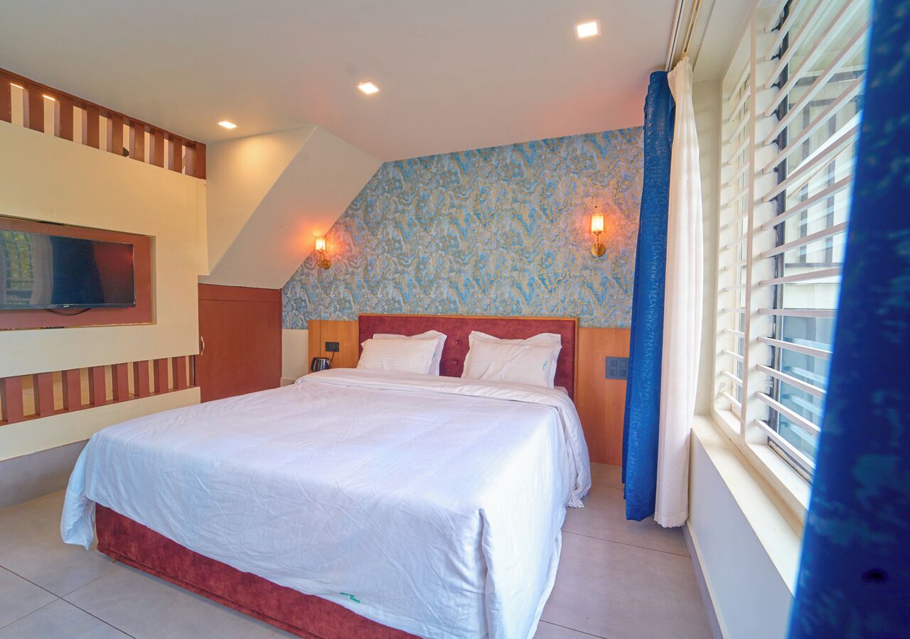Un dormitorio con cama, televisor montado en la pared y ventana con persianas.