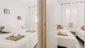 A hotel room with two beds, a bedside table with a lamp, a picture on the wall, and a window with sheer curtains. - Spectacular apartment (Cap d'Artrutx)