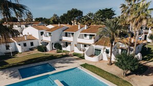A resort with multiple white buildings, a central swimming pool, and palm trees. - Spectacular apartment (Cap d'Artrutx)