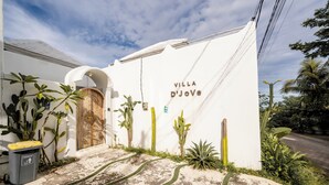 Una villa llamada 'Villa D'JoVe' con fachada blanca, una puerta de madera y un camino que conduce a la entrada.