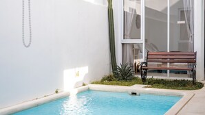 Una piscina pequeña con un banco, un cactus y una pared blanca.