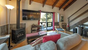 A cozy living room with a fireplace, a sofa, a table, and a TV. - Tramway Haus Mountain Views (Stateline)