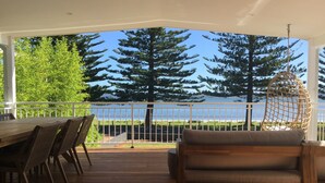 Eine überdachte Terrasse mit Holztisch und -stühlen, einer gepolsterten Bank und Blick auf ein Gewässer und Bäume.