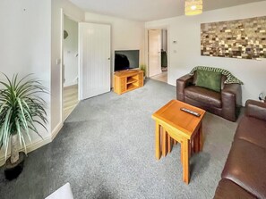 A living room with a brown leather sofa, a wooden coffee table, a TV stand, and a potted plant.