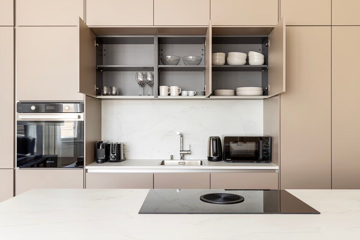 A modern kitchen with built-in appliances, a marble countertop, and open shelving with dishes and glasses.