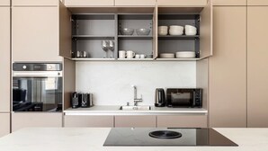 Een moderne keuken met inbouwapparatuur, een marmeren aanrechtblad en open planken met servies en glazen.