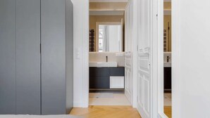 Een slaapkamer met een bed, een grijze garderobe en een open deur naar een badkamer met een wastafel en spiegel.