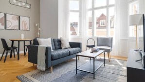 Een moderne woonkamer met een bank, salontafel en stoelen, grote ramen en uitzicht naar buiten.