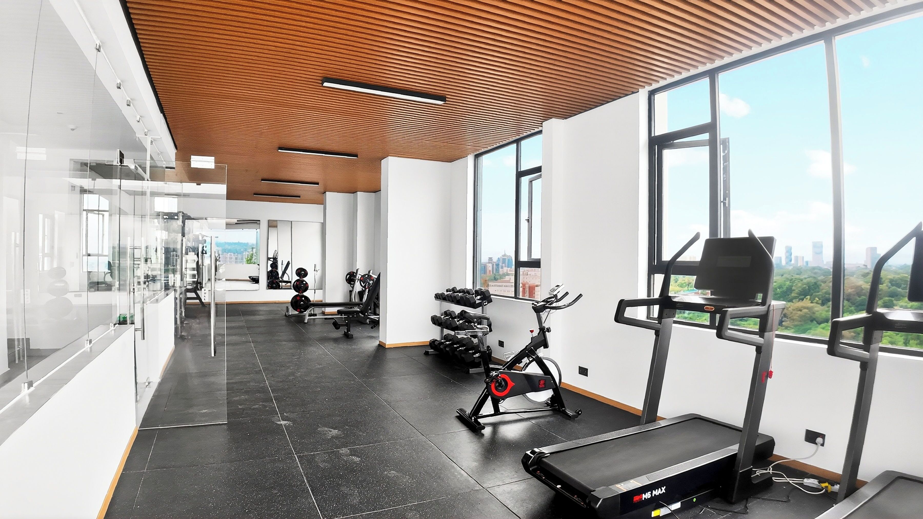 Ein Fitnessstudio mit Trainingsgeräten, großen Fenstern und Blick auf die Stadt.