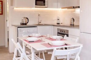 Una cocina moderna con muebles blancos, un microondas y un comedor con sillas blancas y una mesa dispuesta para dos personas.