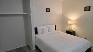 A bedroom with a bed, a nightstand with a lamp, and two wall decorations. - Spacious 3 Bedroom Private Guest Suite (Inuvik)