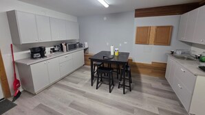 A compact kitchen with white cabinets, a dining table with chairs, a coffee maker, and a microwave. - Spacious 3 Bedroom Private Guest Suite (Inuvik)