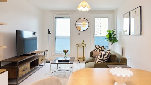 A modern living room with a flat-screen TV, a coffee table, a sofa, and a dining table. - The Fifth Above Hackney (London)