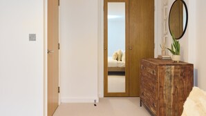 A bedroom with a wooden wardrobe, a mirror, and a bed with a white duvet. - The Fifth Above Hackney (London)