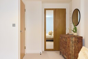 A bedroom with a wooden wardrobe, a mirror, and a bed with a white duvet. - The Fifth Above Hackney (London)