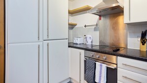 A kitchen with white cabinets, a stainless steel range hood, a toaster, and a kettle. - The Fifth Above Hackney (London)