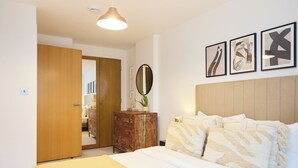 A bedroom with a bed, wooden dresser, mirror, and wall art. - The Fifth Above Hackney (London)