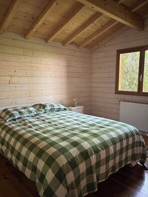 Un dormitorio con cama, paredes de madera, ventana y radiador.