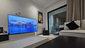 Ett modernt vardagsrum med en stor platt-TV, en soffa, ett soffbord och en glasdörr som leder ut till en balkong.