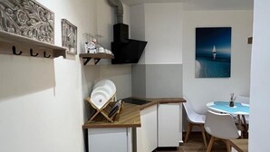 Una cocina compacta con horno integrado, un refrigerador pequeño y una zona de comedor con una mesa redonda y sillas.