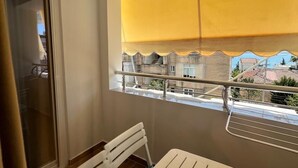 Un balcón con una mesa y sillas, una ventana con persiana amarilla y vistas a edificios.