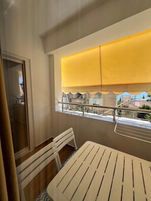 Ein Balkon mit Tisch und Stühlen, ein Fenster mit gelbem Rollo und Blick auf Gebäude.