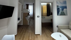 Una habitación de hotel moderna con televisión, literas, zona de comedor, una pequeña mesa y obras de arte en las paredes.