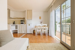Eine moderne Küche mit weißen Geräten, ein Essbereich mit weißem Tisch und Stühlen sowie eine große Schiebeglastür, die auf einen Balkon führt.