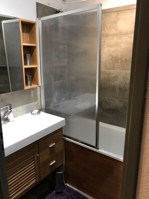 Ein Badezimmer mit weißem Waschbecken, einem Spiegel, einer Duschkabine und Holzschränken.