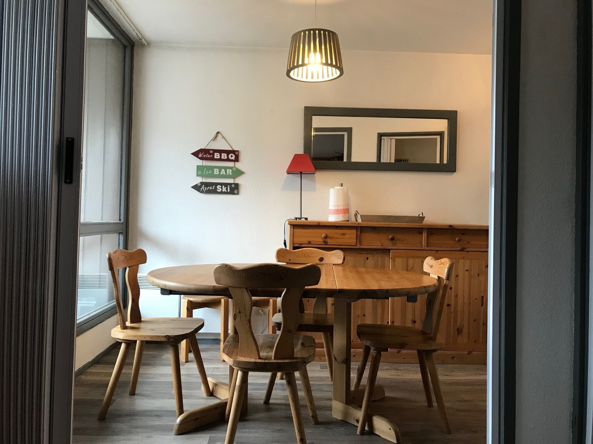 Ein Essbereich mit Holztisch und -stühlen, einer Hängeleuchte, einem Spiegel und Hinweisschildern an der Wand.
