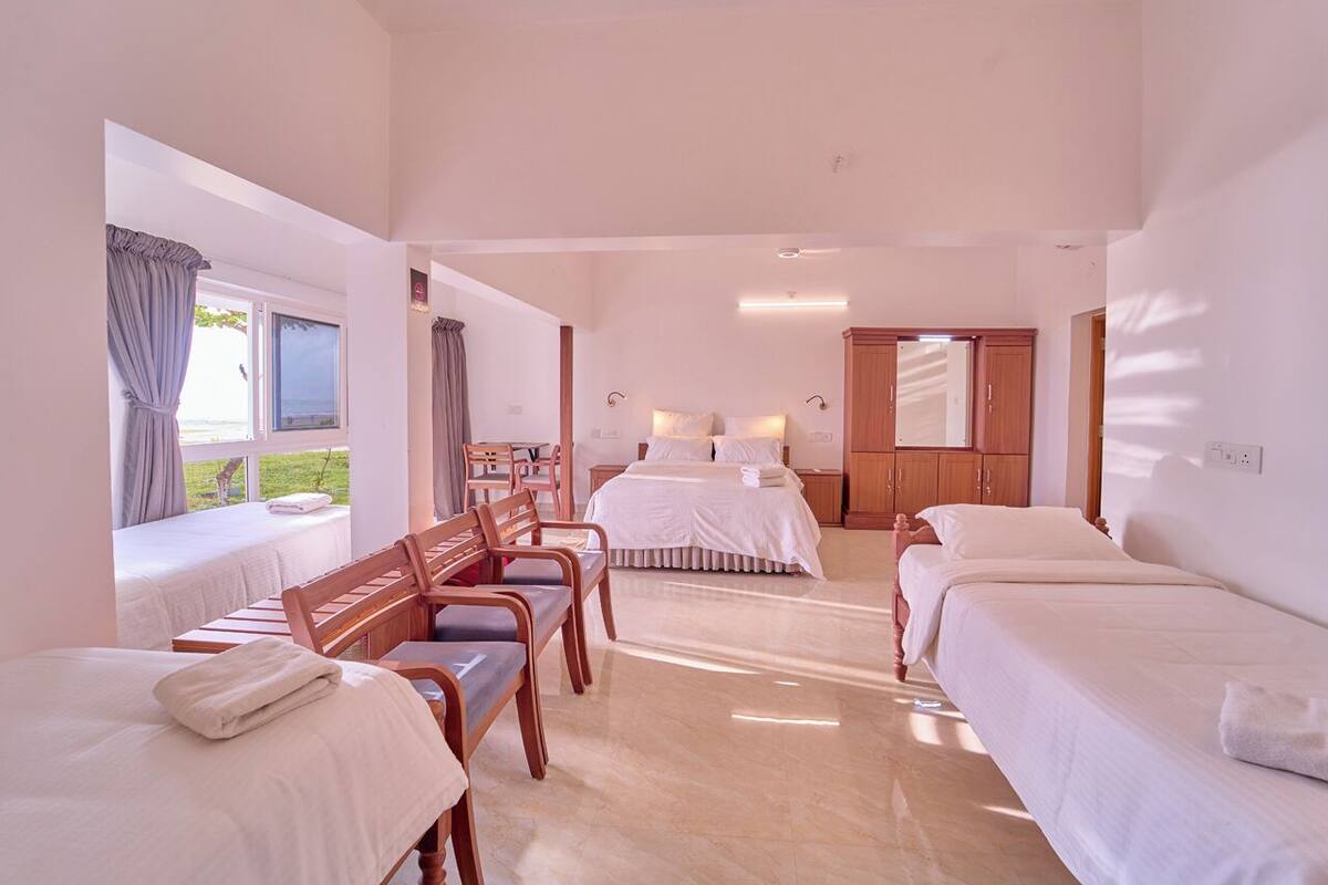 A hotel room with two beds, a wooden bench, a desk, and a view of the outdoors.