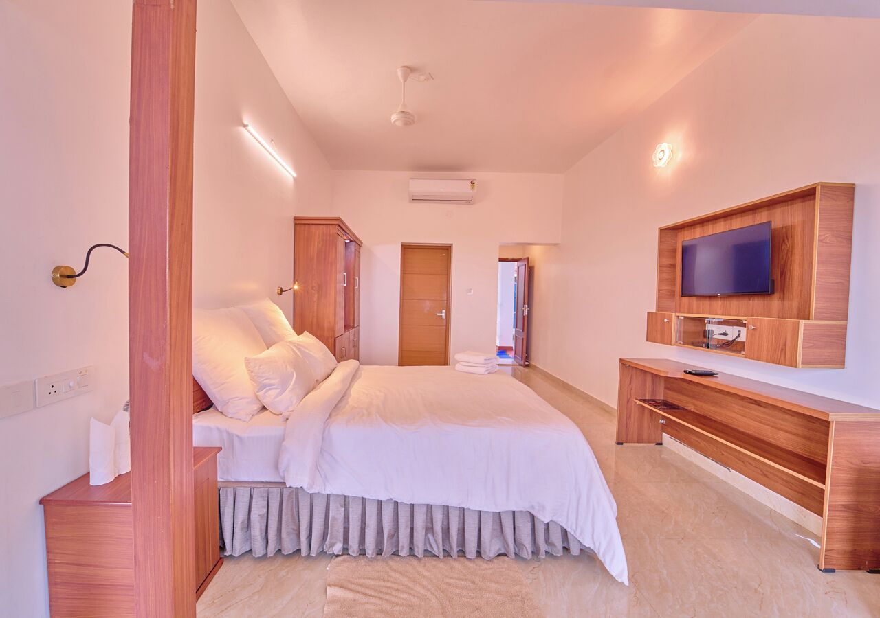 A bedroom with a bed, wooden furniture, a TV, and an air conditioning unit.