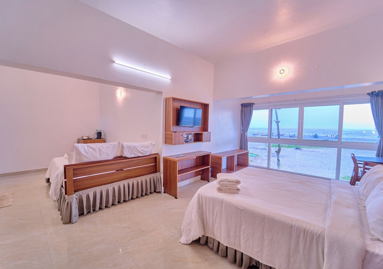Une chambre d’hôtel avec un lit, un bureau, une télévision et une vue sur la plage.