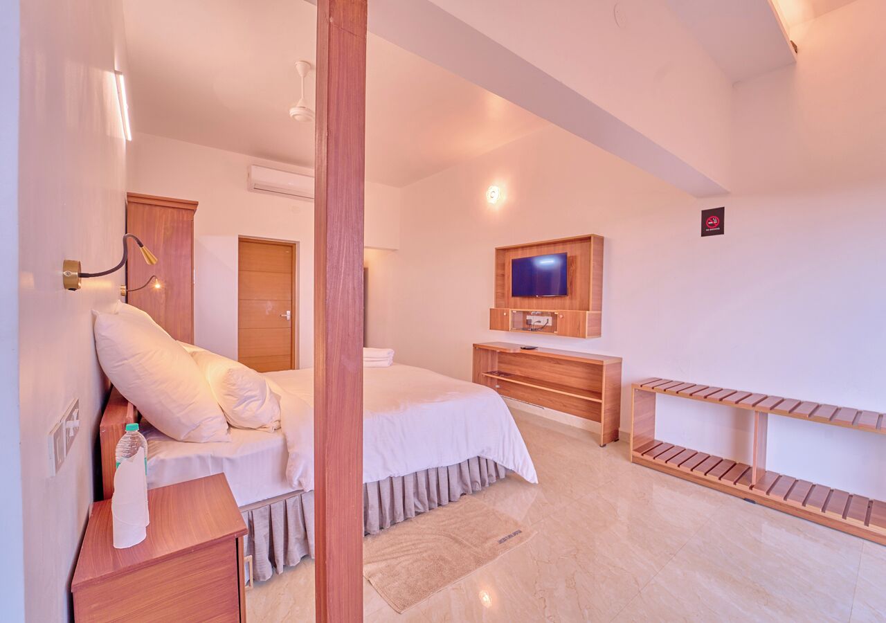 A hotel room with a bed, a wooden dresser, a TV, and a shoe rack.