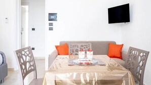 Een eethoek met een tafel voor twee personen, een bank met oranje kussens en een wandmontage flatscreen televisie.